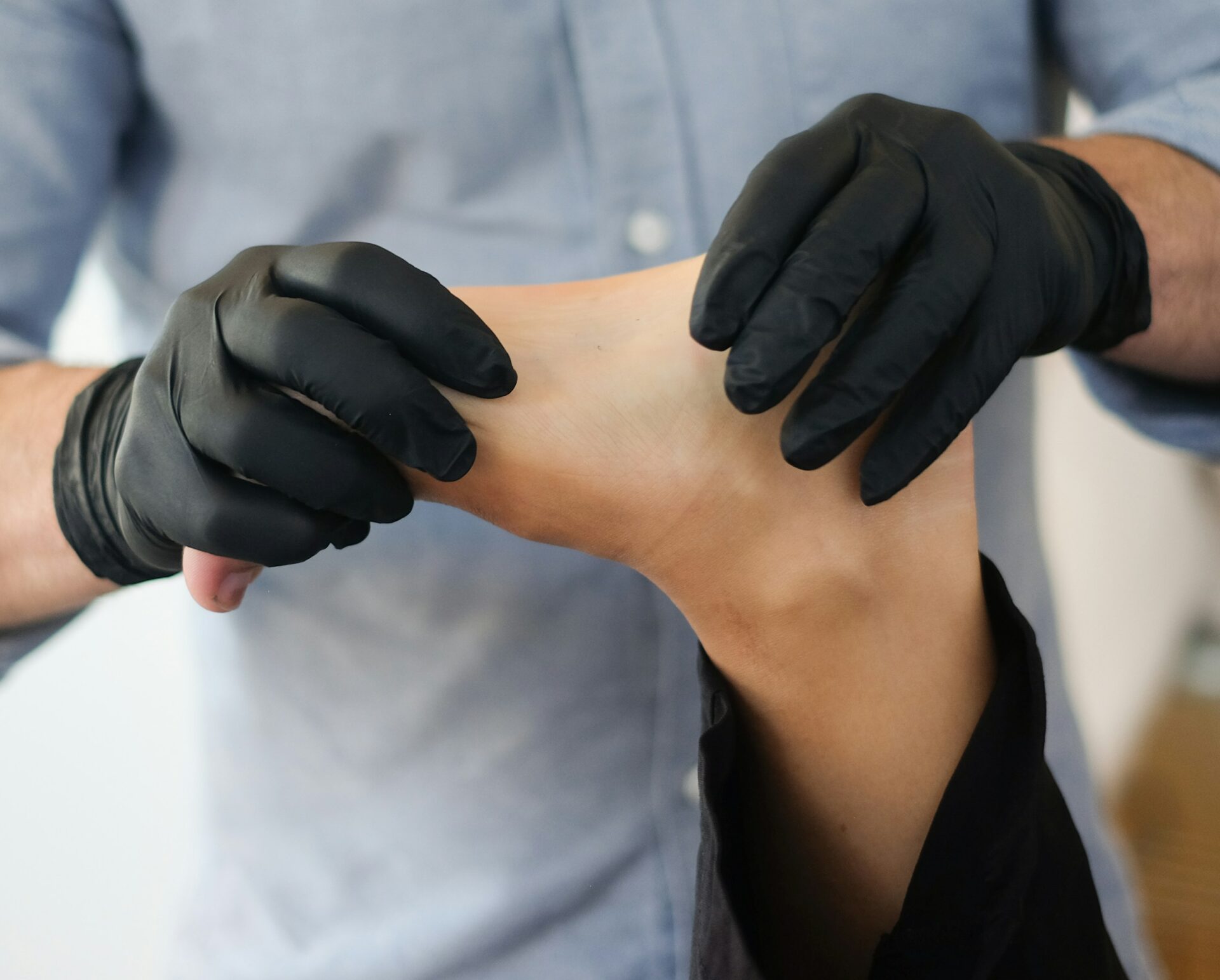 A close-up of a physiologist providing a therapeutic foot massage while wearing black gloves.